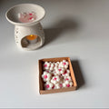White ceramic wax warmer with a candle and a box of wax melts on a light gray surface.