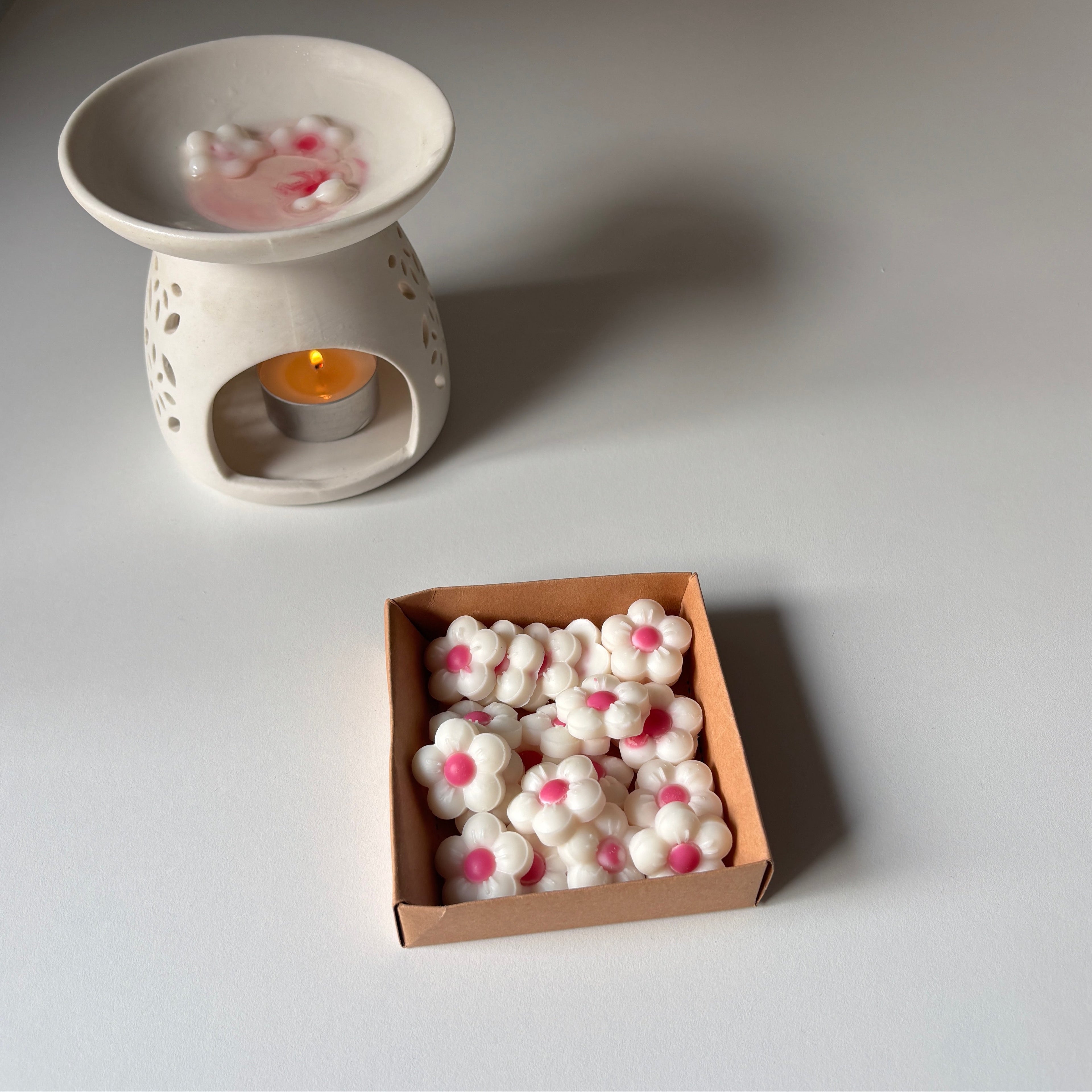 White ceramic wax warmer with a candle and a box of wax melts on a light gray surface.