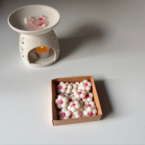 White ceramic wax warmer with a candle and a box of wax melts on a light gray surface.