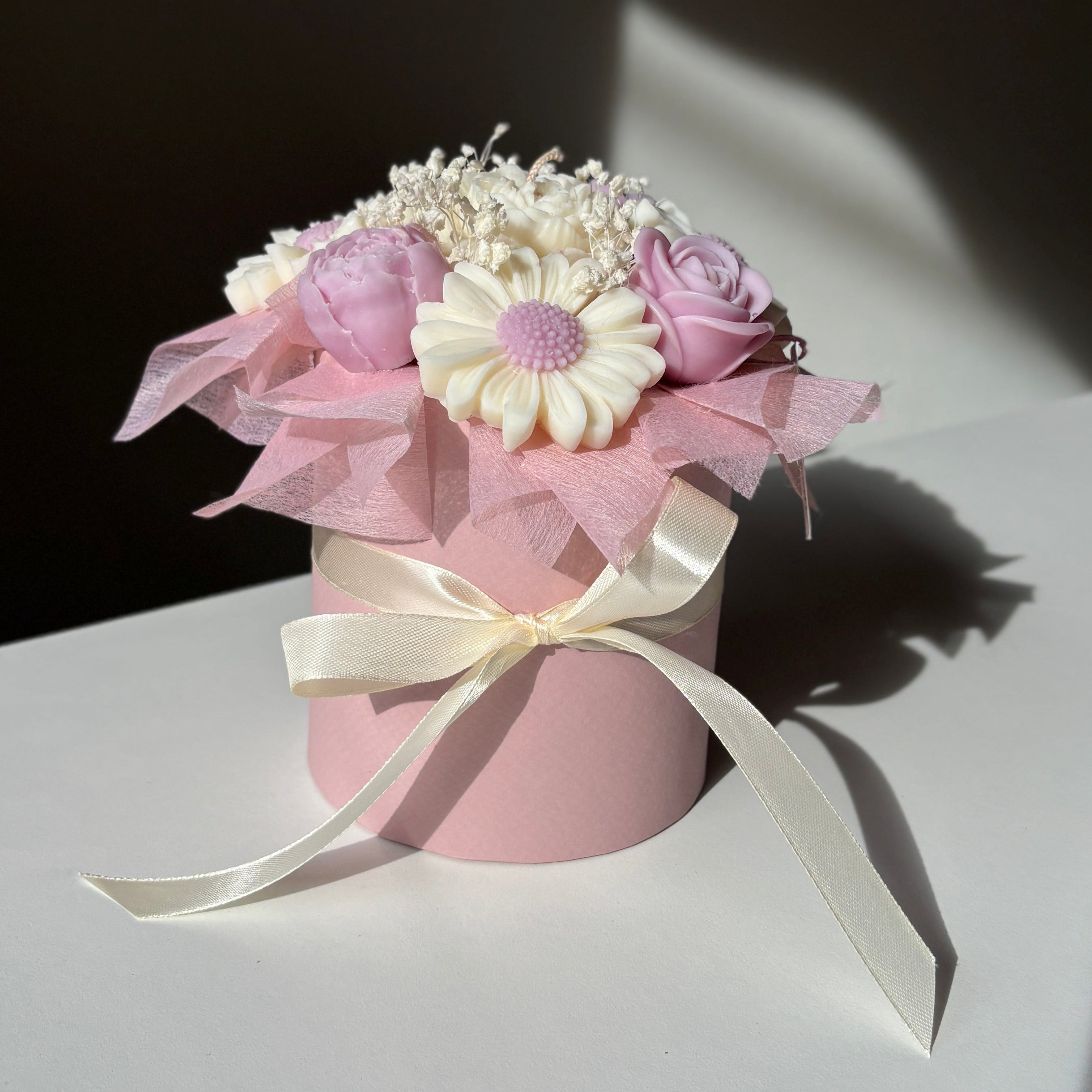 Small pink vase with flowers and ribbons on a white surface