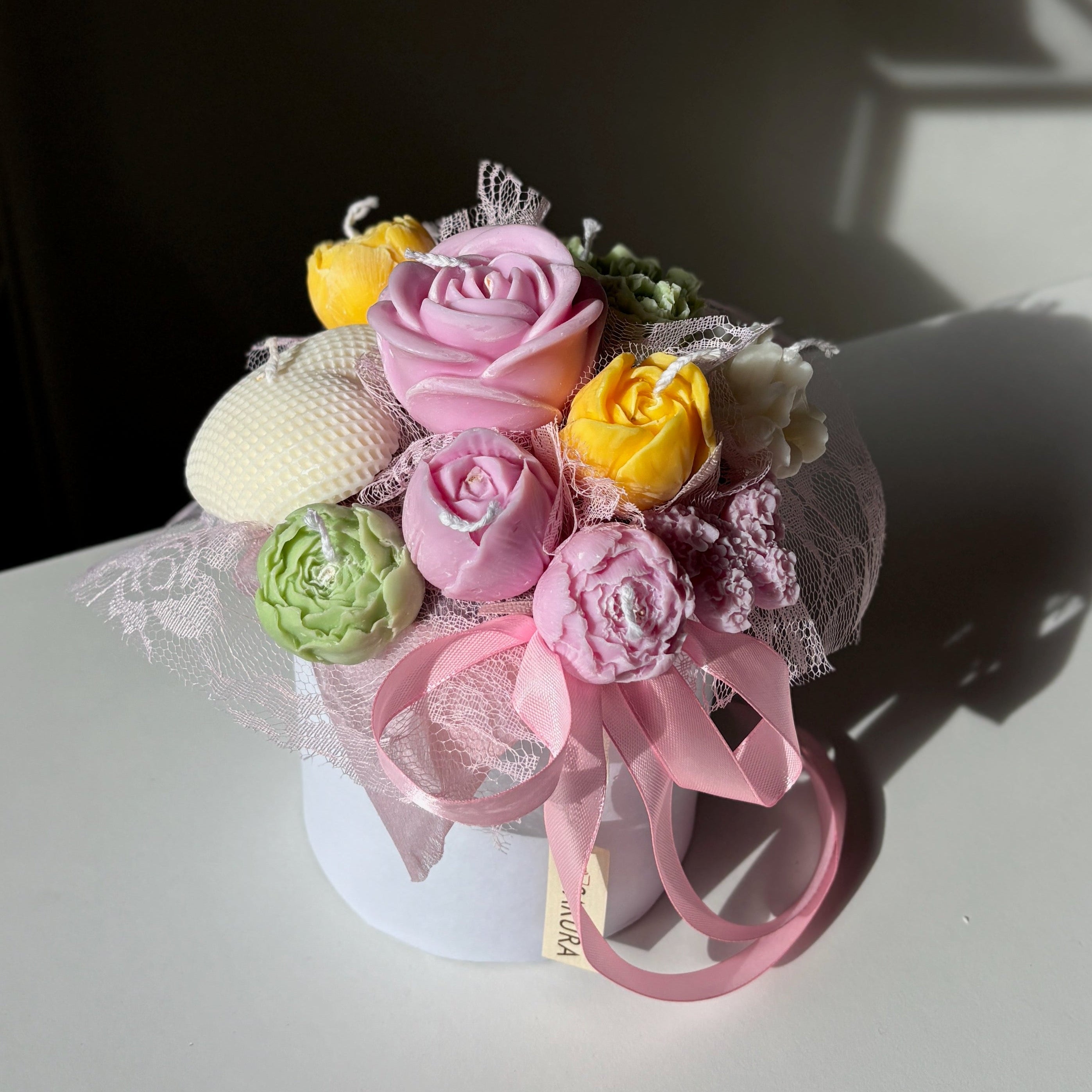 Small bouquet of flowers in a clear container with pink ribbon on a white surface.