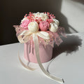 Decorative flower arrangement in a pink container on a white surface with a dark background