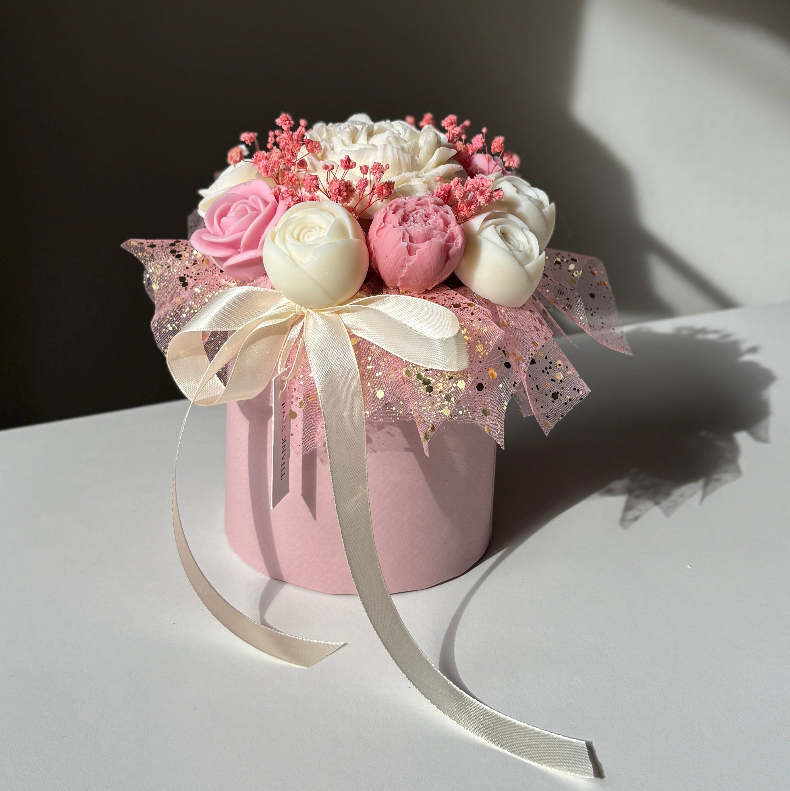 Decorative flower arrangement in a pink container on a white surface with a dark background
