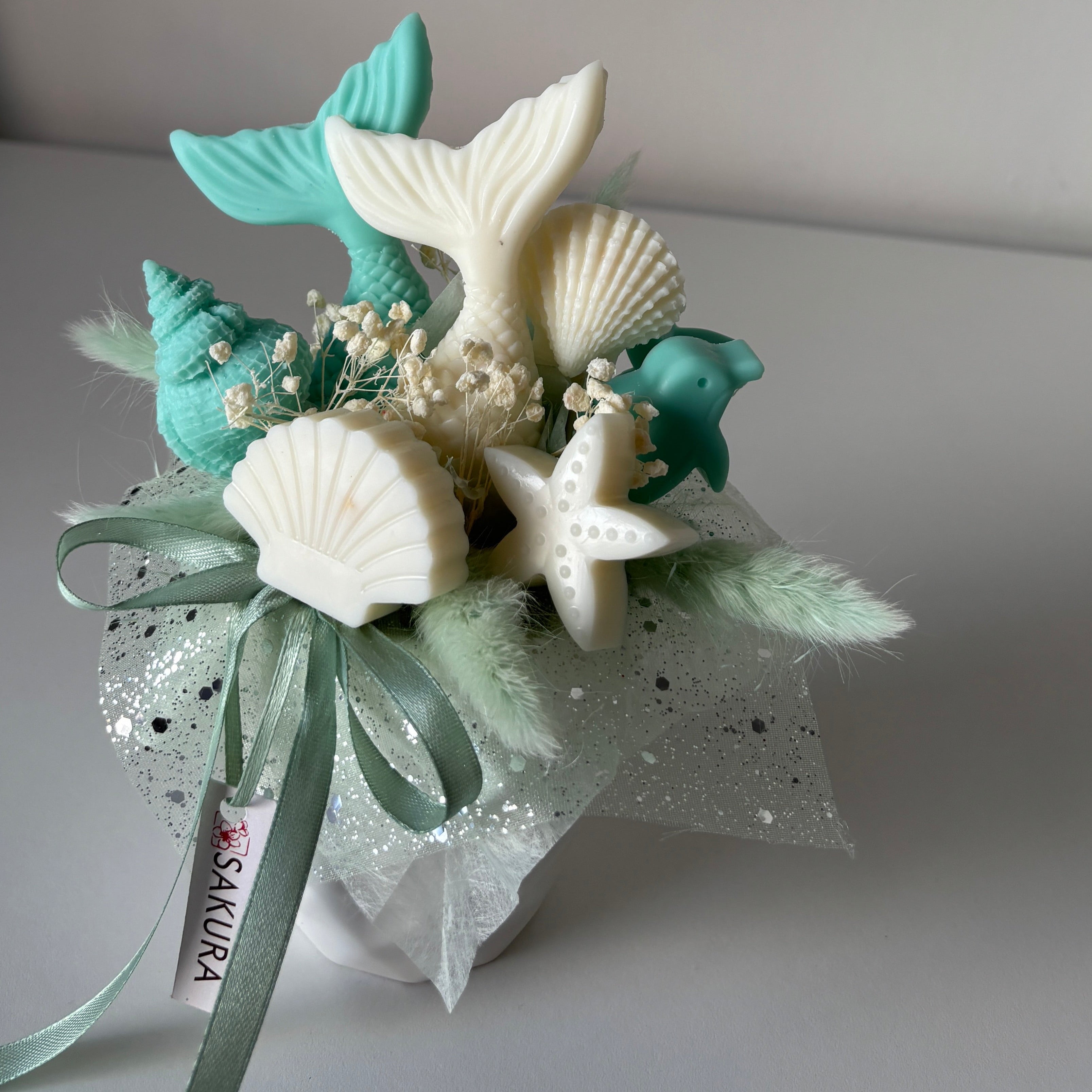 Decorative corsage with mermaid tail, shells, and starfish on a plain background